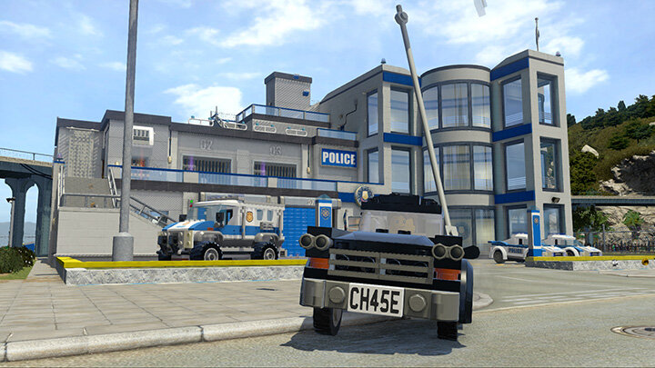 Posterunek policji Lego z zaparkowanym przed nim samochodem Lego. Błękitne niebo w tle.