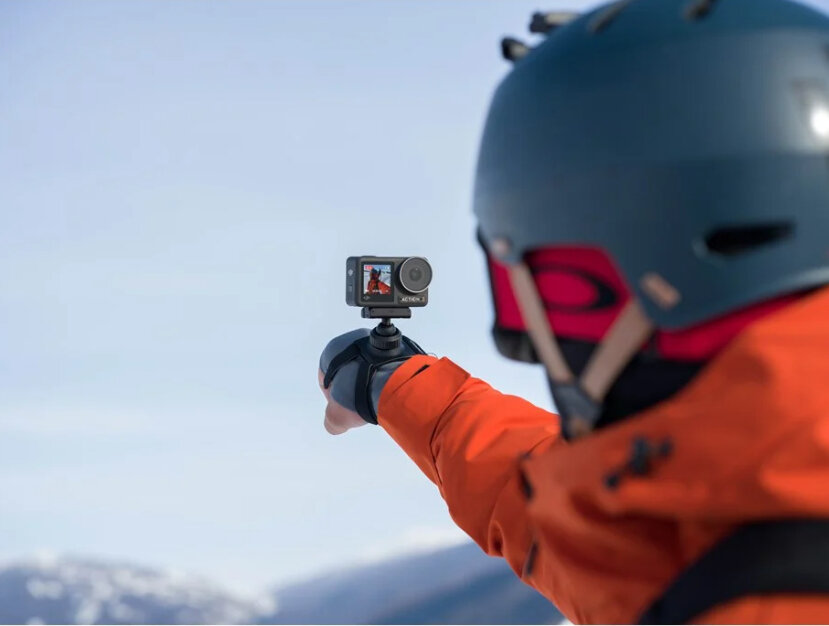 Osoba w kurtce i kasku trzyma kamerę, filmując na tle błękitnego nieba.