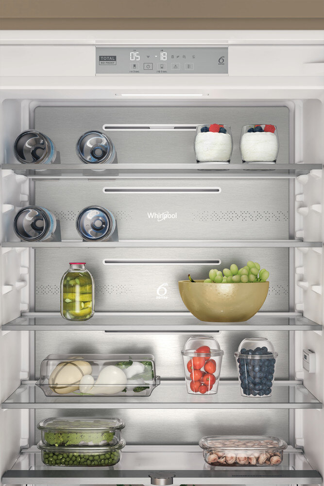 Lodówka z różnymi produktami spożywczymi ułożonymi na półkach, w tym napojami, owocami i warzywami.