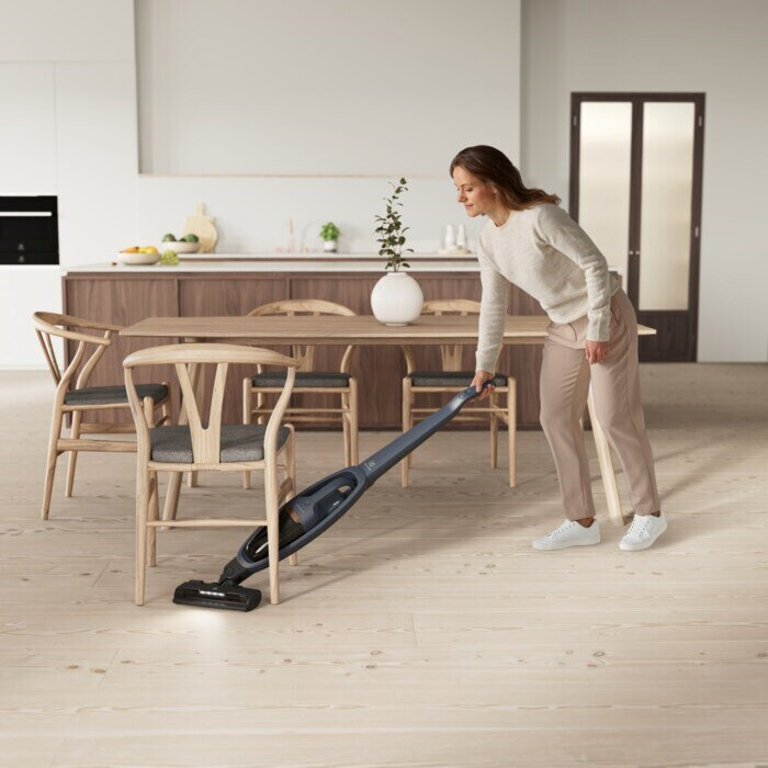 Kobieta odkurzająca drewnianą podłogę odkurzaczem bezprzewodowym we współczesnym domu.
