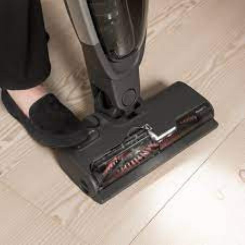 Czarna głowica odkurzacza na drewnianej podłodze. Stopa spoczywa na głowicy.