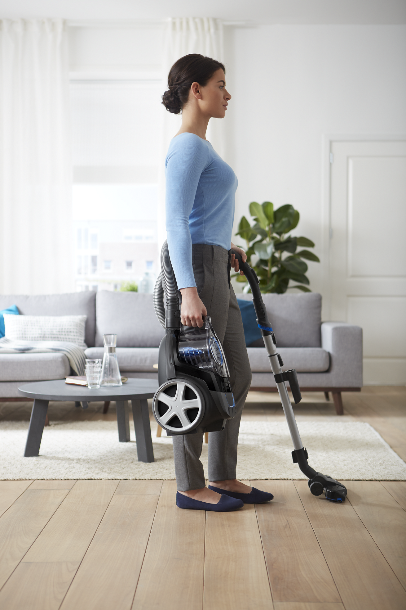 Kobieta z odkurzaczem w salonie z drewnianą podłogą.