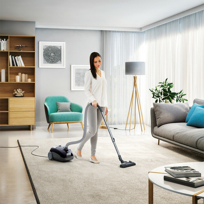 Kobieta odkurza dywan w salonie z nowoczesnymi meblami.