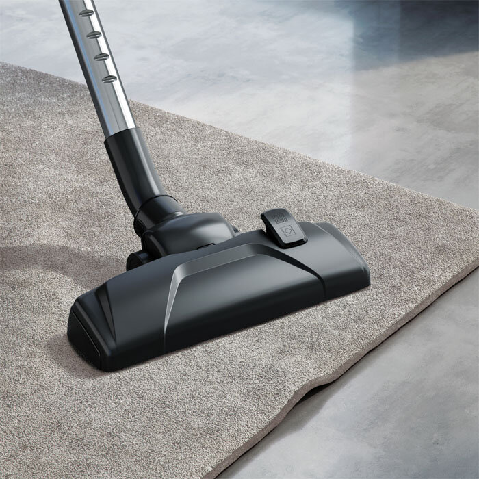 Czarna głowica odkurzacza czyści szary dywan na betonowej podłodze.