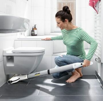Kobieta czyszcząca podłogę w łazience za pomocą odkurzacza Kärcher. Widoczna toaleta i umywalka.