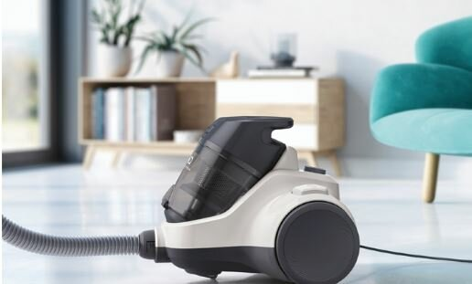 Biały i czarny odkurzacz stoi na podłodze. W tle szafka i turkusowe krzesło.