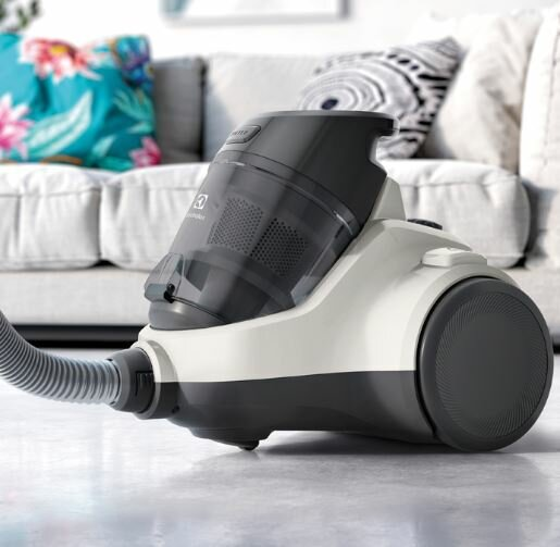 Biało-szary odkurzacz Electrolux na szarej podłodze, obok sofy.