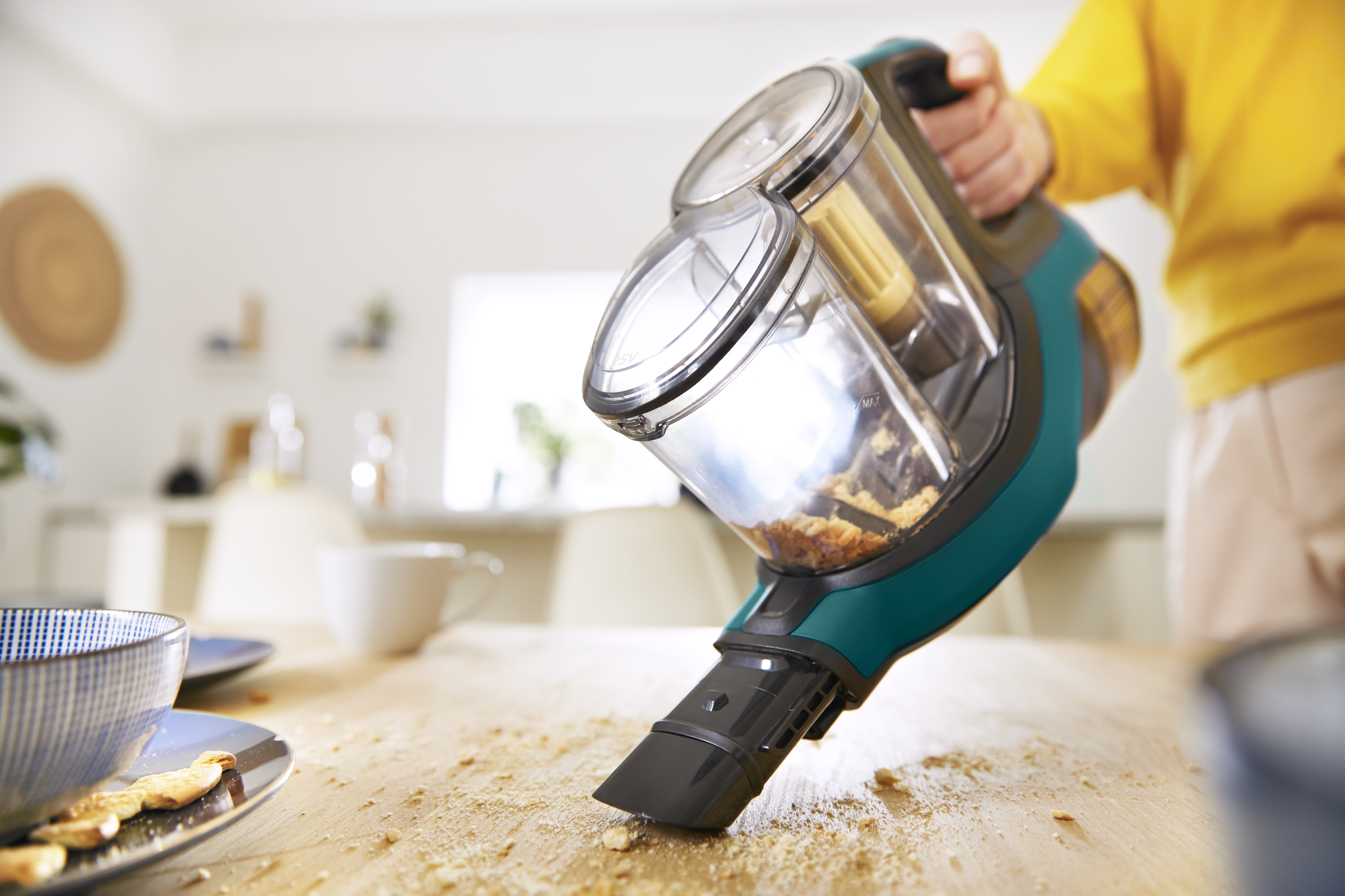 Osoba używająca odkurzacza ręcznego na drewnianym stole z okruchami.