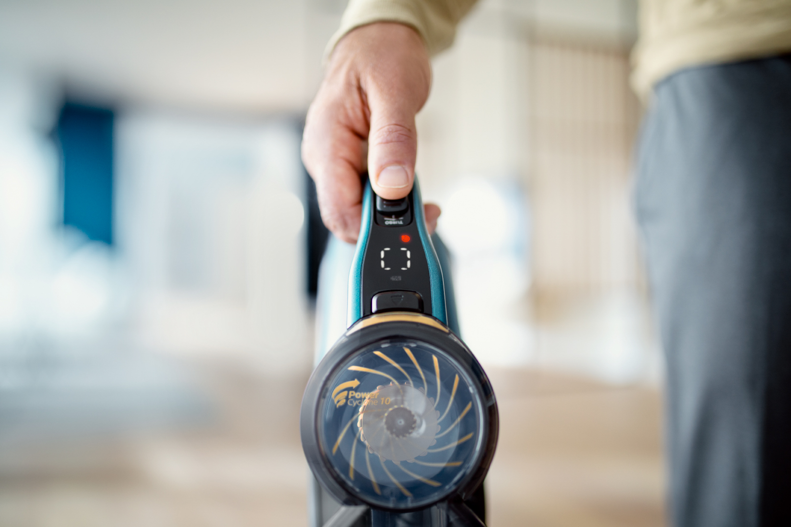 Dłoń trzymająca czarno-niebiesko-zielony odkurzacz, zbliżenie na przód.