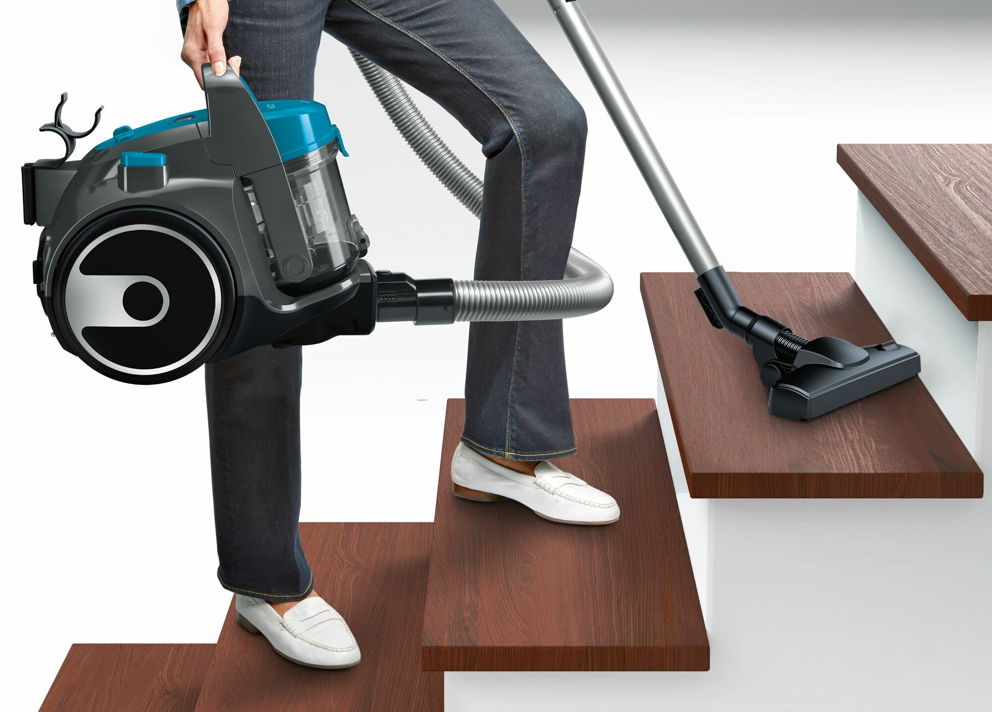Osoba odkurza schody. Trzyma odkurzacz i używa węża i dyszy.
