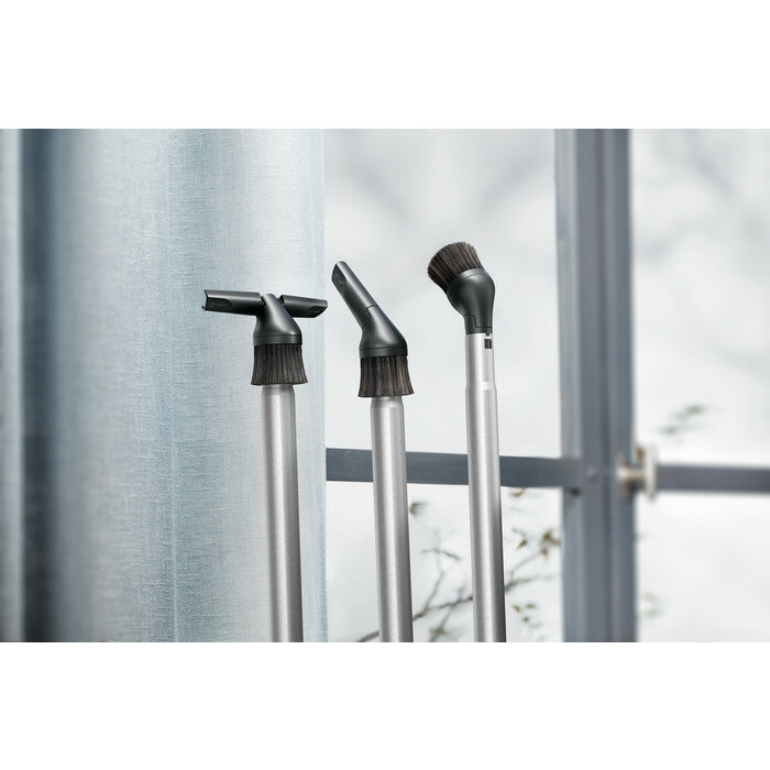 Trzy nasadki do odkurzacza przed oknem. Mają czarne włosie i srebrne trzpienie.