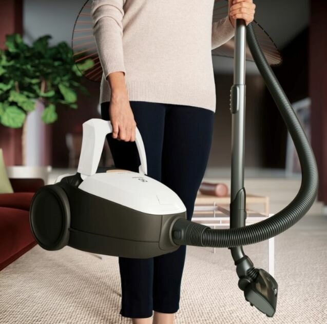Kobieta trzymająca odkurzacz. Jest biało-czarny, z wężem i głowicą czyszczącą.