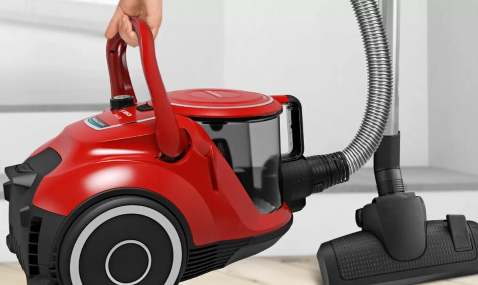 Czerwony odkurzacz z uchwytem i wężem. Ręka osoby trzyma uchwyt.