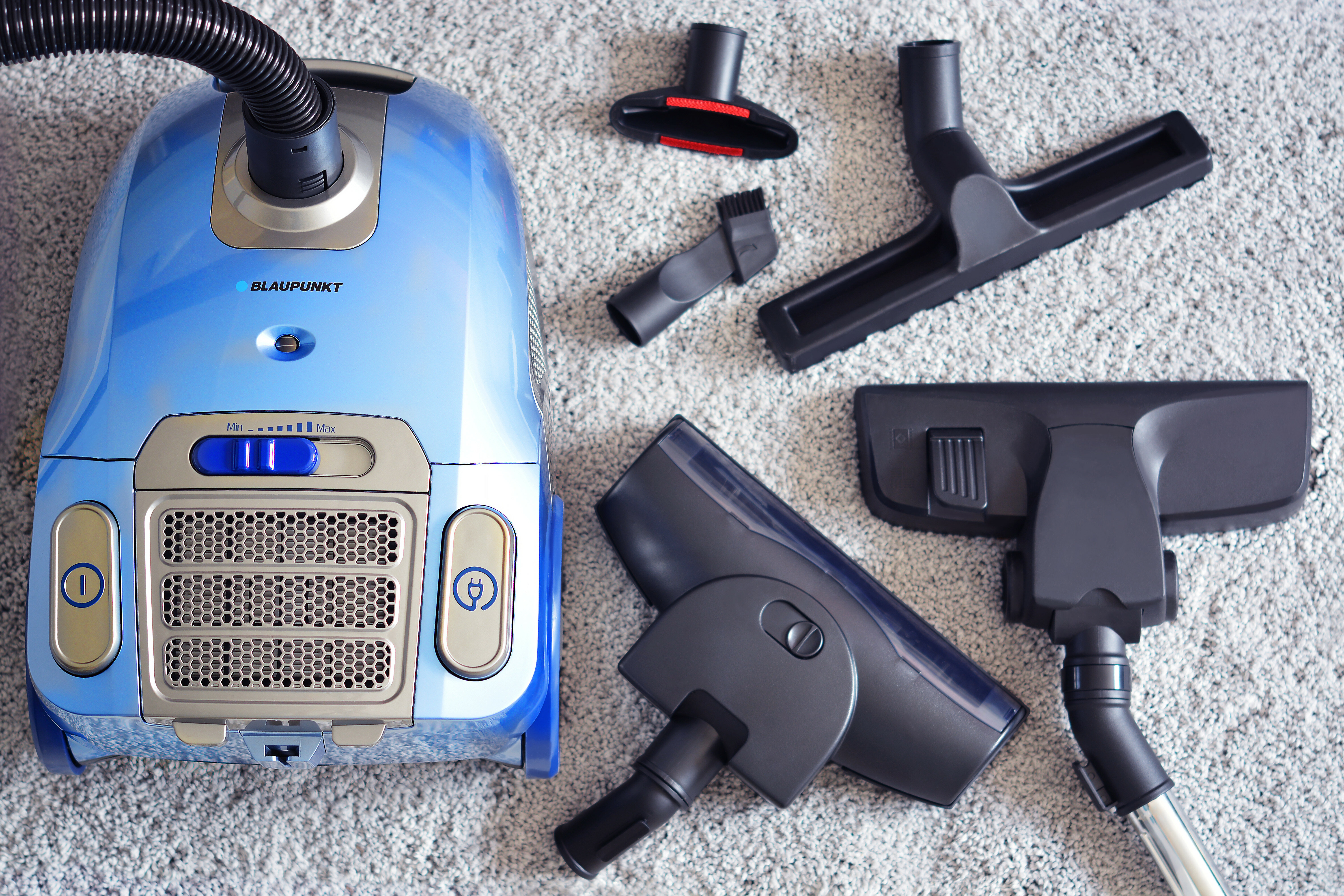 Niebieski odkurzacz z akcesoriami. Ułożono różne dysze i szczotki.