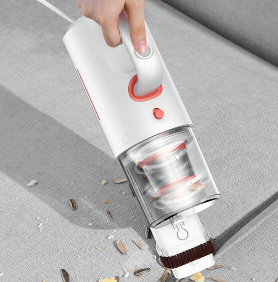 Osoba odkurza kanapę. Używa małego, białego odkurzacza z nasadką szczotkową.