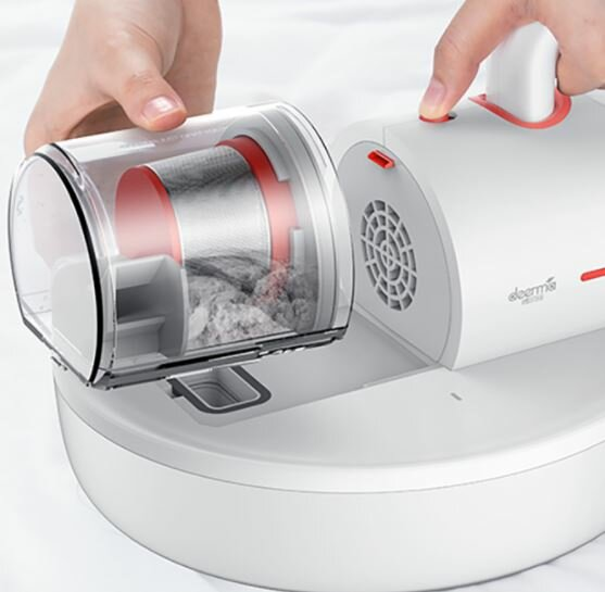 Ręce wyjmują pojemnik na kurz z białej podstawy odkurzacza, odsłaniając zebrane zanieczyszczenia.