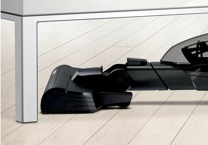 Głowica odkurzacza pod stołem. Głowica jest czarna, a podłoga drewniana.