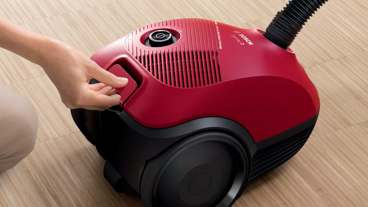 Czerwony odkurzacz z ręką kobiety otwierającą komorę na drewnianej podłodze.