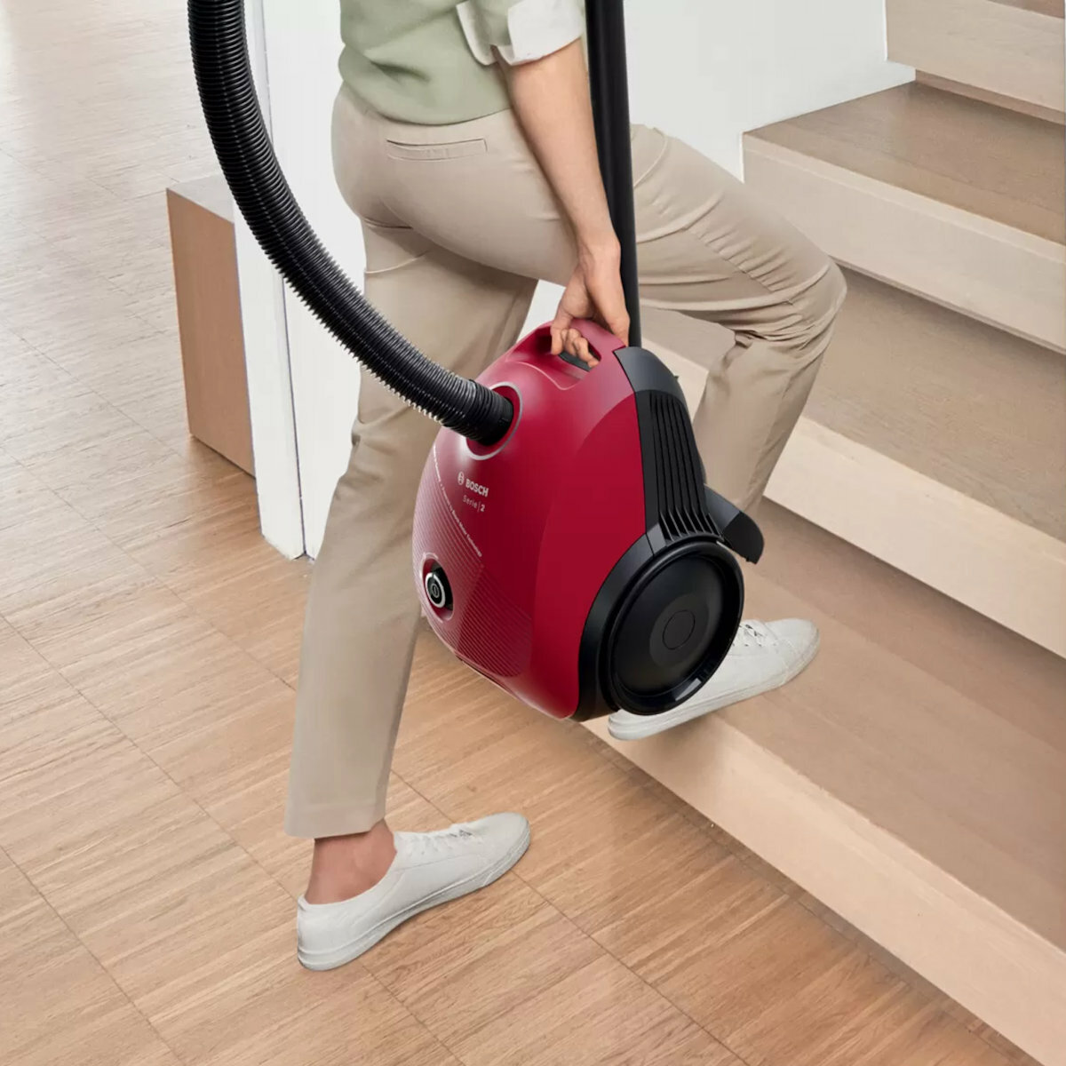 Osoba niosąca czerwony odkurzacz po schodach.