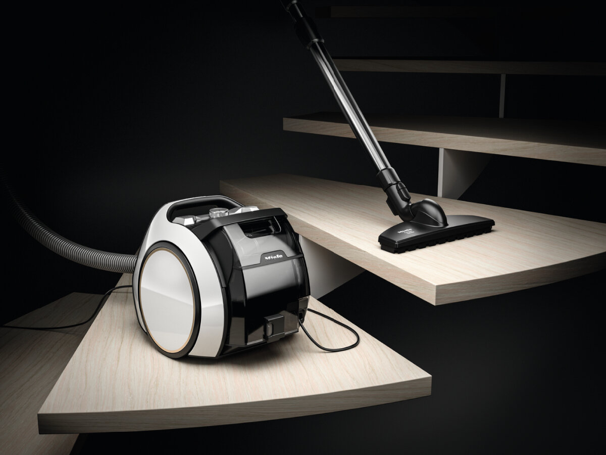Czarno-biały odkurzacz na drewnianych schodach. Wąż jest rozłożony.