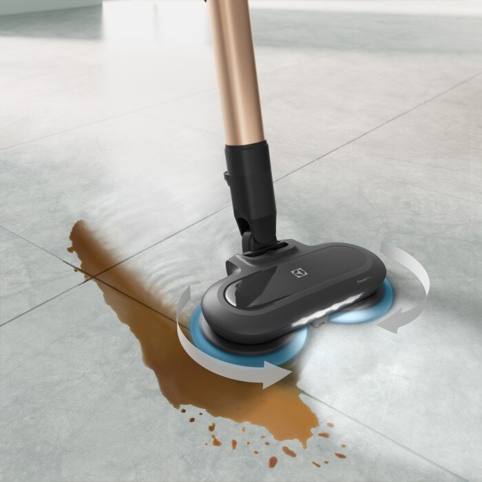 Odkurzacz czyści plamę brązowego płynu na szarej podłodze z płytek.