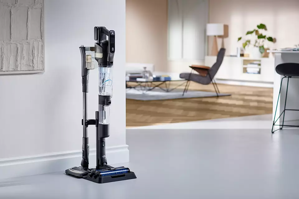 Pionowy odkurzacz i jego akcesoria, stojące przy białej ścianie.