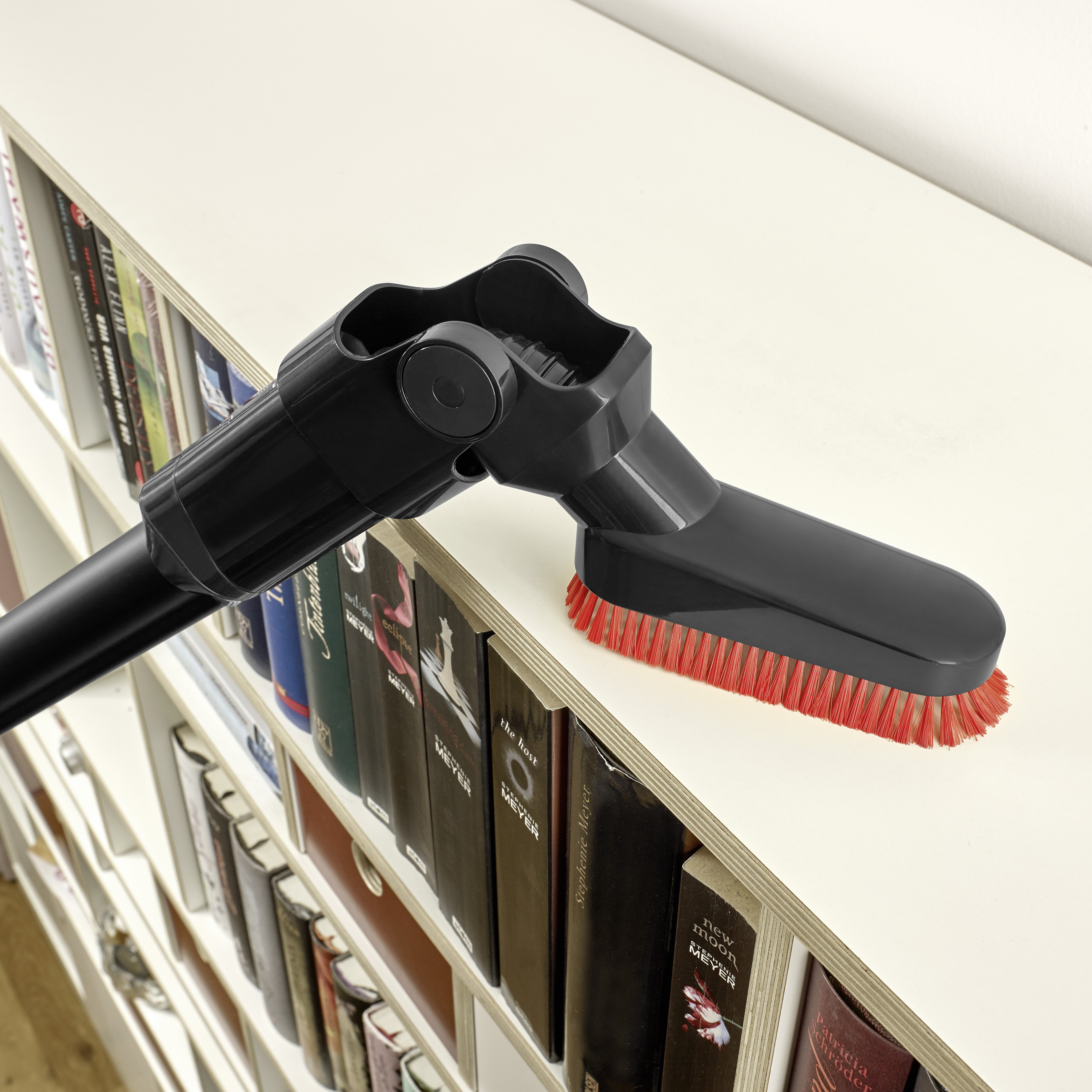 Głowica szczotki odkurzacza czyszcząca półkę na książki z czerwonym włosiem.