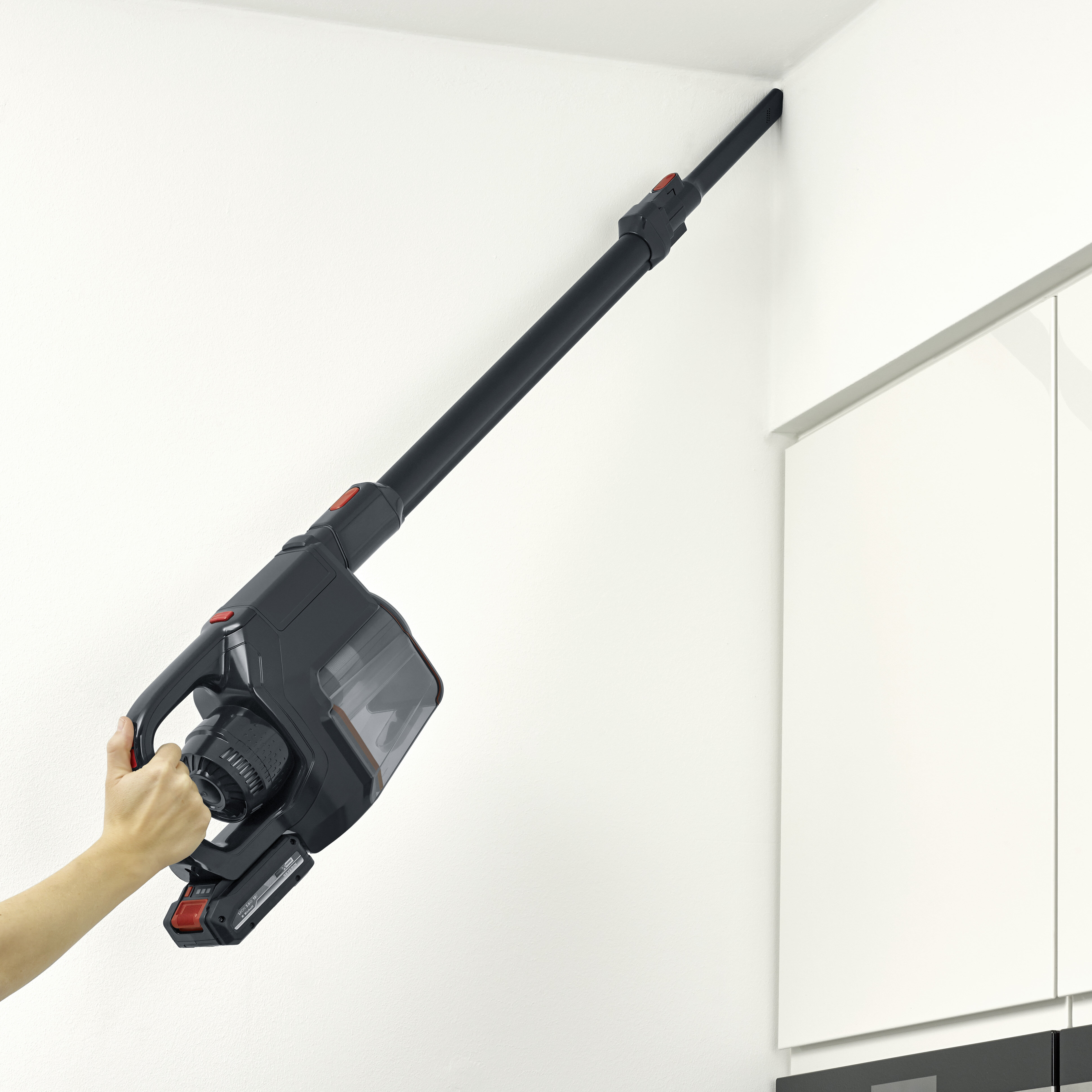 Czarny i szary odkurzacz trzymany jest na białej ścianie.