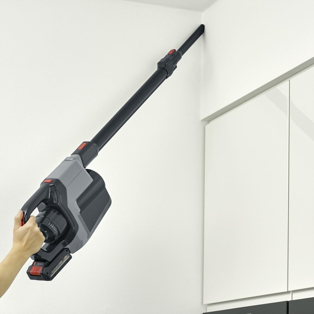 Ręka trzyma odkurzacz przy białej ścianie. Odkurzacz jest czarny i szary.
