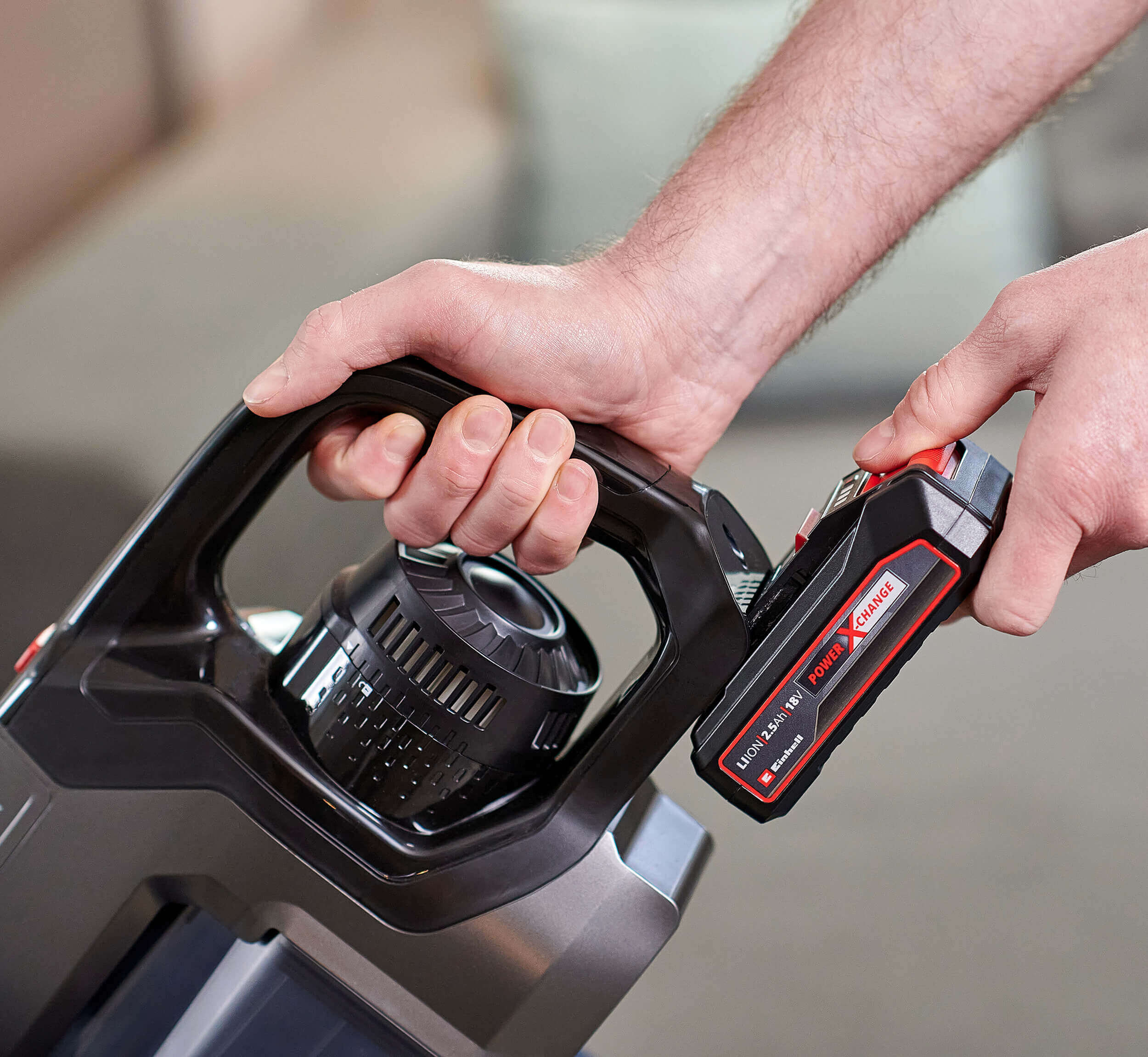 Ręka wkłada czarną baterię do czarno-szarego odkurzacza bezprzewodowego.