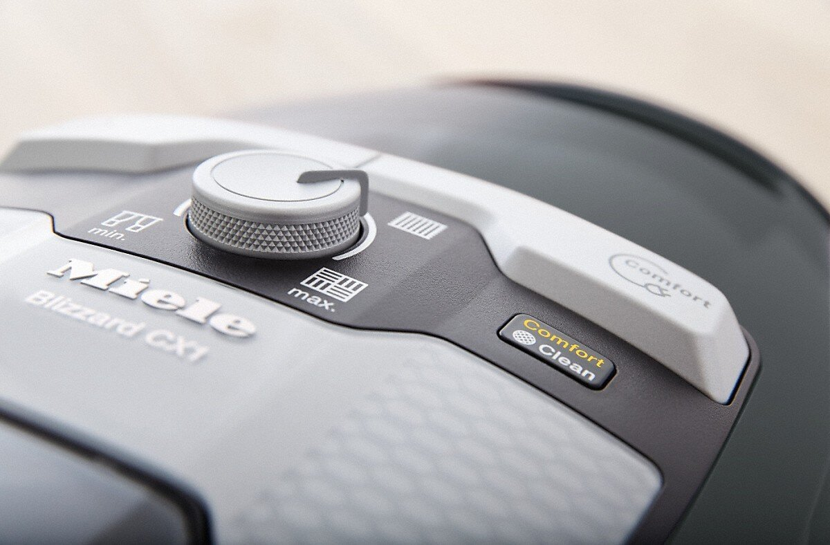 Zbliżenie panelu sterowania odkurzacza z przyciskami i pokrętłem. Marka to Miele.