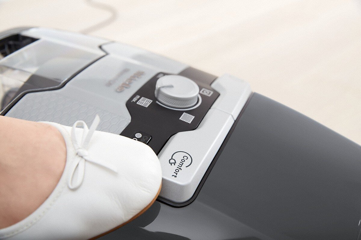 Stopa osoby naciskająca przycisk na szarym odkurzaczu.