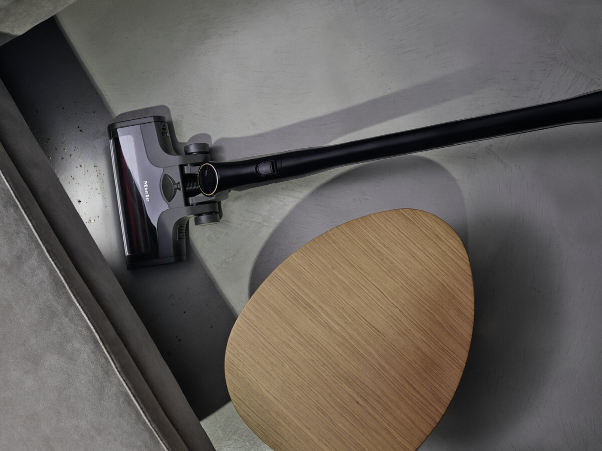 Odkurzacz i drewniany owalny stół na szarej powierzchni. Ciemne tło.