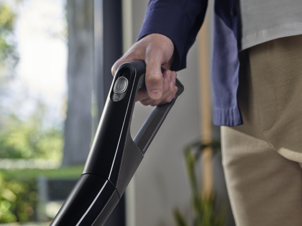 Dłoń osoby trzymająca czarną część odkurzacza. Osoba ma na sobie granatową kurtkę.