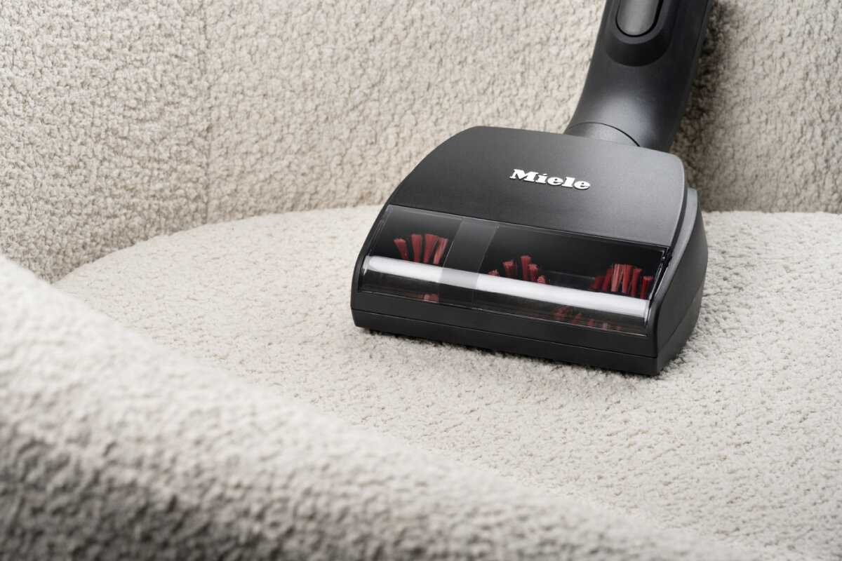 Głowica odkurzacza na beżowej kanapie. Widoczna czerwona szczotka. Widok z bliska.