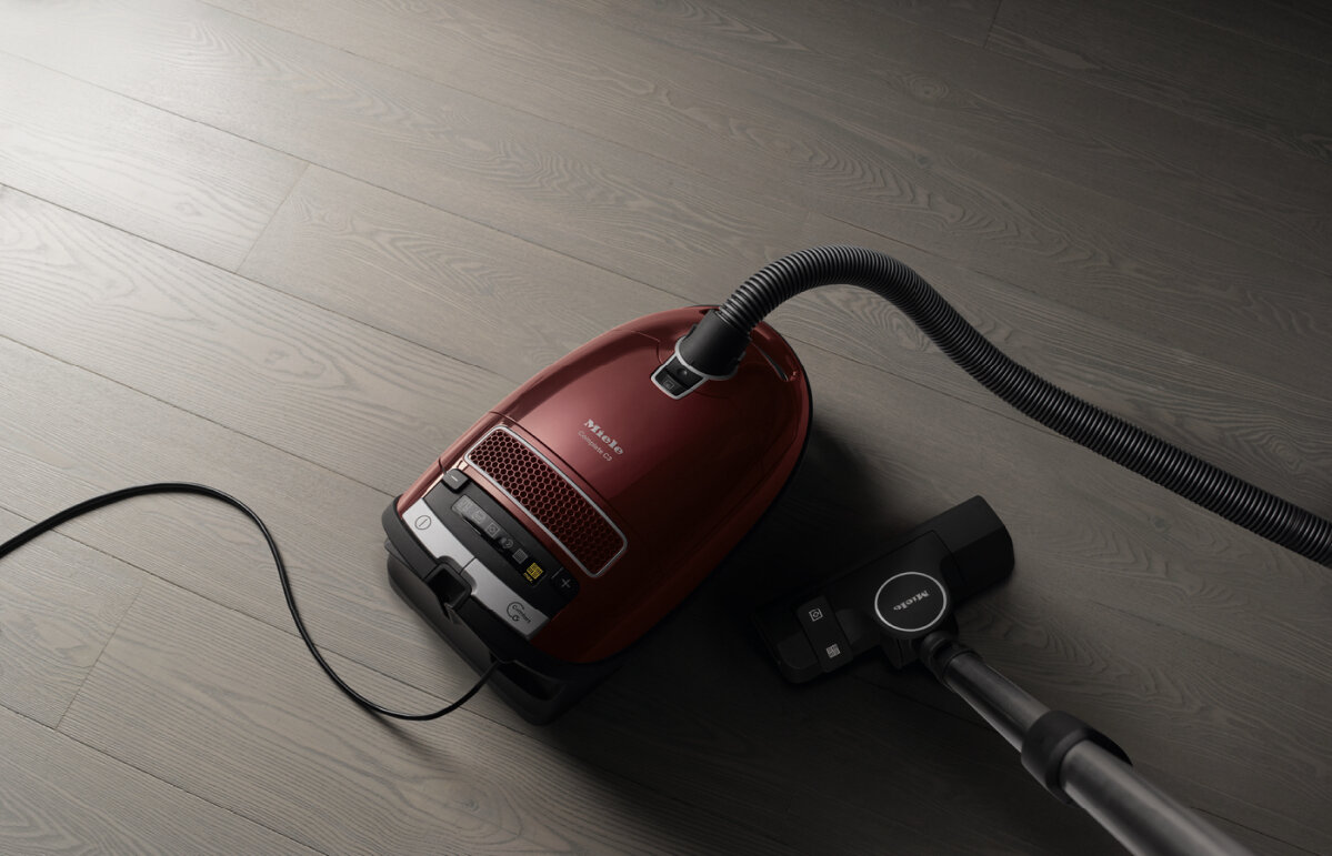Czerwony odkurzacz na drewnianej podłodze. Czarny wąż i czarny osprzęt są podłączone do odkurzacza.