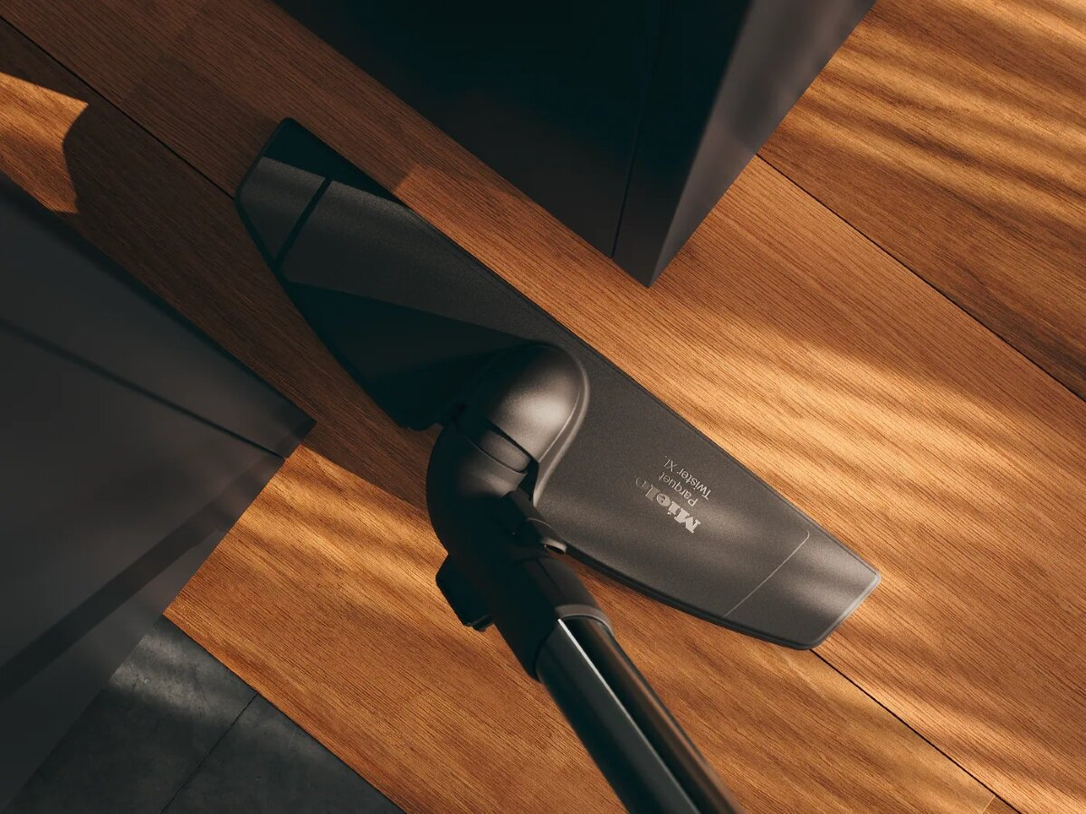 Głowica odkurzacza na drewnianej podłodze. Tło przedstawia podłogę i ciemną ścianę.