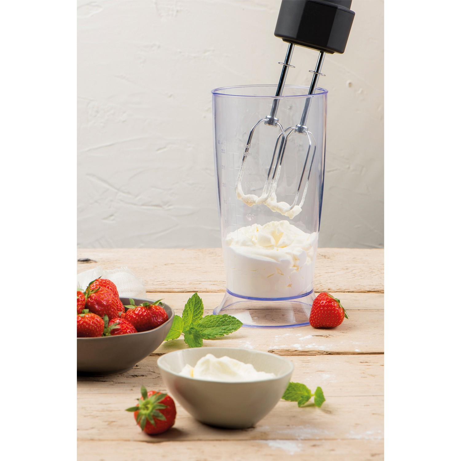Mixer in een hoog glas met slagroom, aardbeien en munt op een houten tafel.