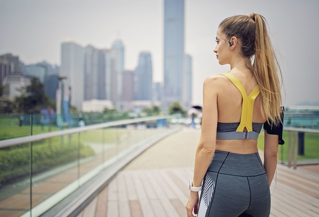 Una mujer en ropa deportiva mira una ciudad desde un puente.
