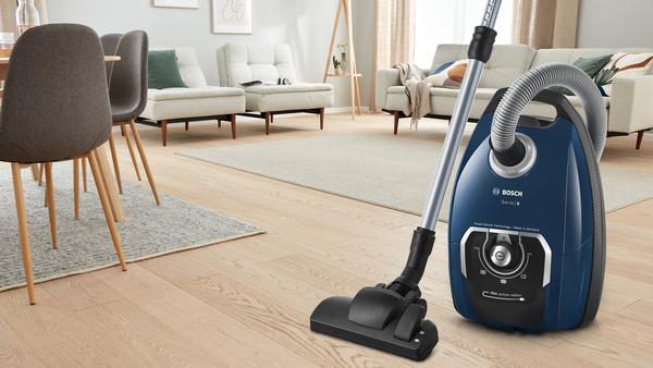 Blauer Staubsauger mit langem Griff auf Holzboden in einem Wohnzimmer.