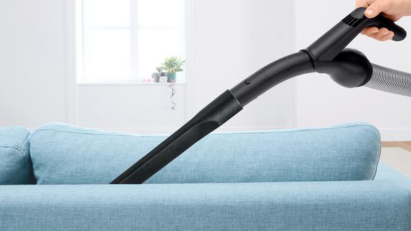 Eine Person, die ein blaues Sofa mit einem schwarzen Staubsaugeraufsatz absaugt.