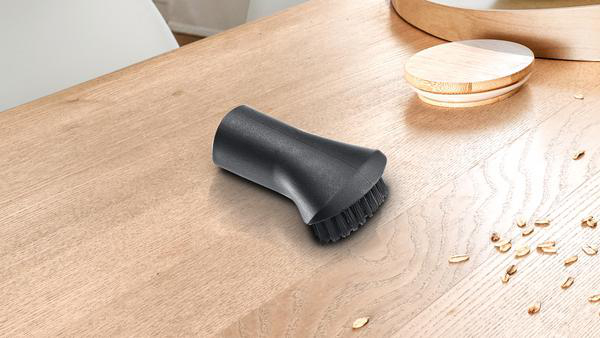 Schwarze Staubsaugerbürste auf Holzoberfläche. Verstreute Getreidekörner.