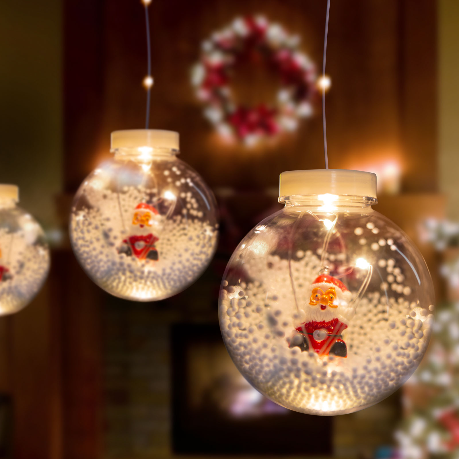 Karácsonyi díszek, bennük Mikulás figurákkal és fehér, hóhoz hasonló részecskékkel.