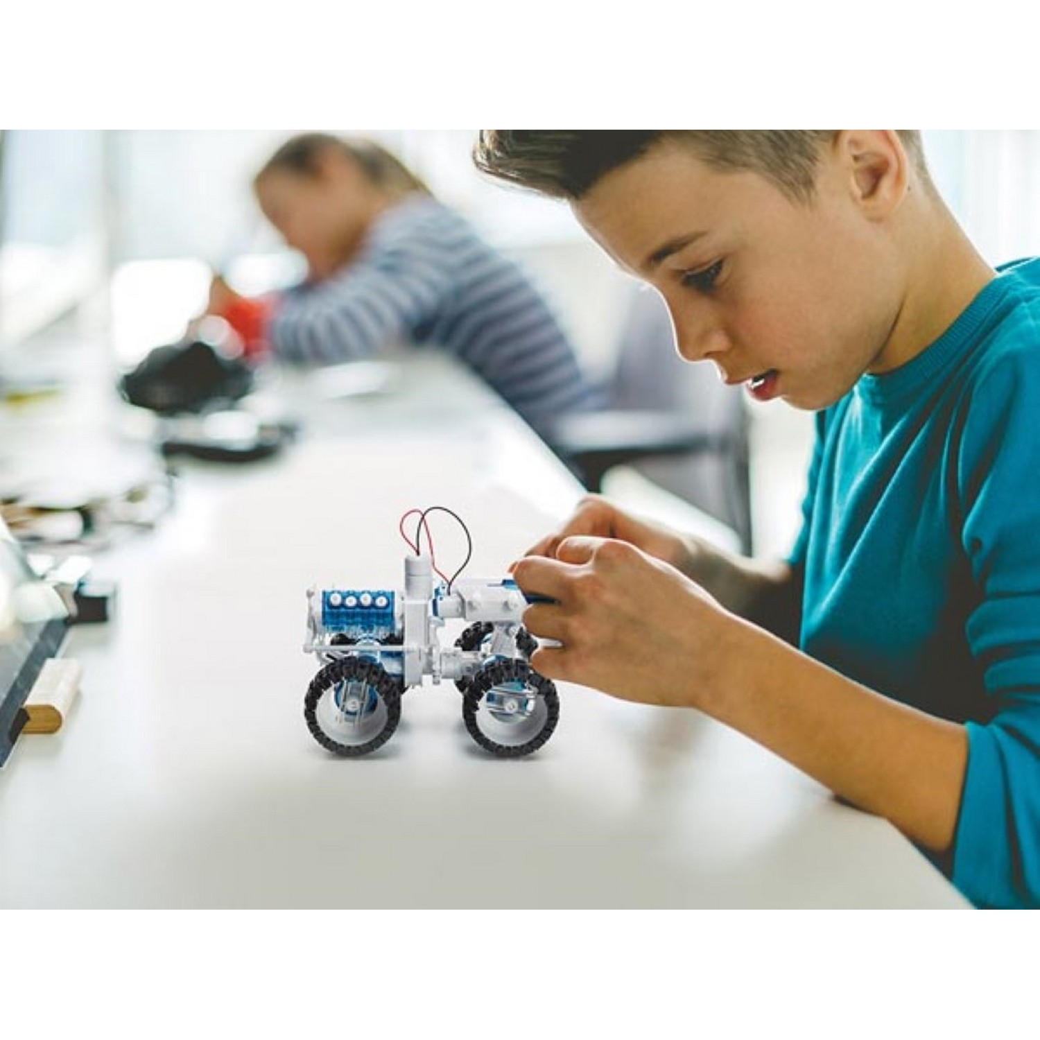Boy and girl building a small toy car together at a table, with a focus on the boy.