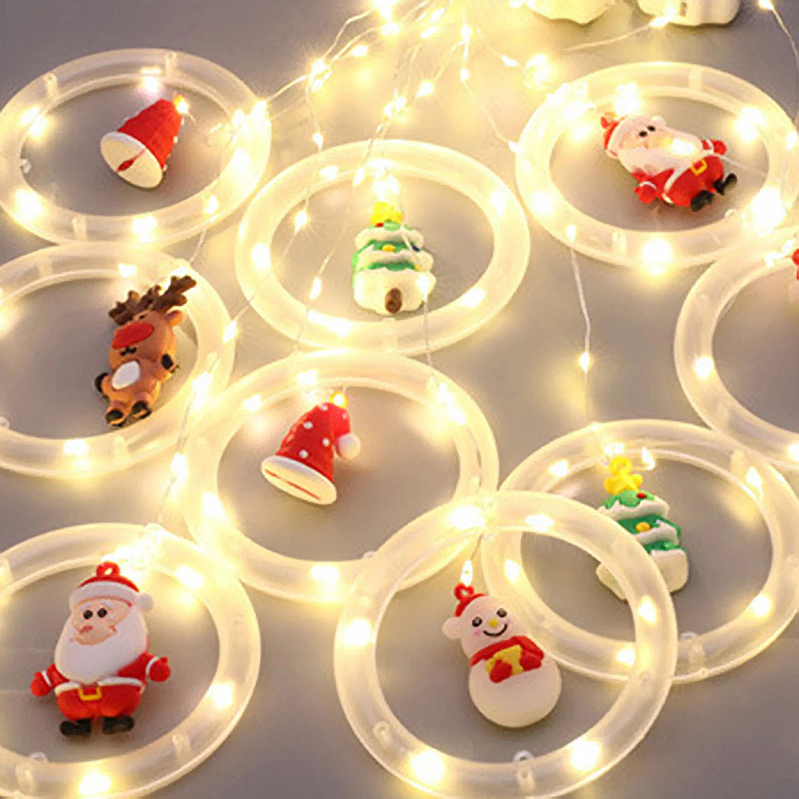 Karácsonyi díszek, beleértve a Mikulást és a hóembert, fehér világító gyűrűk körül, világosszürke felületen.