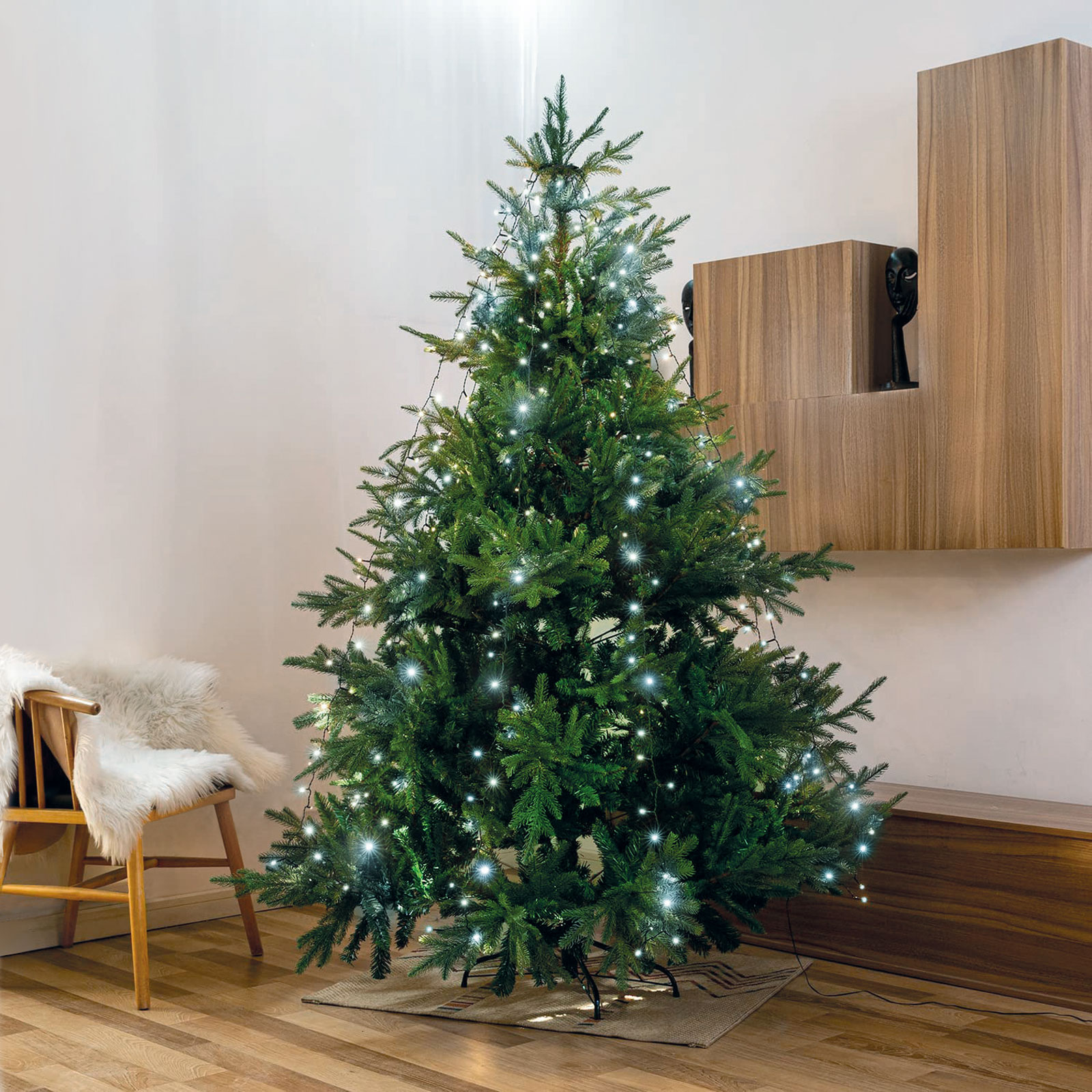 Díszített karácsonyfa fehér fényekkel. Balra egy szék. Fa fal.