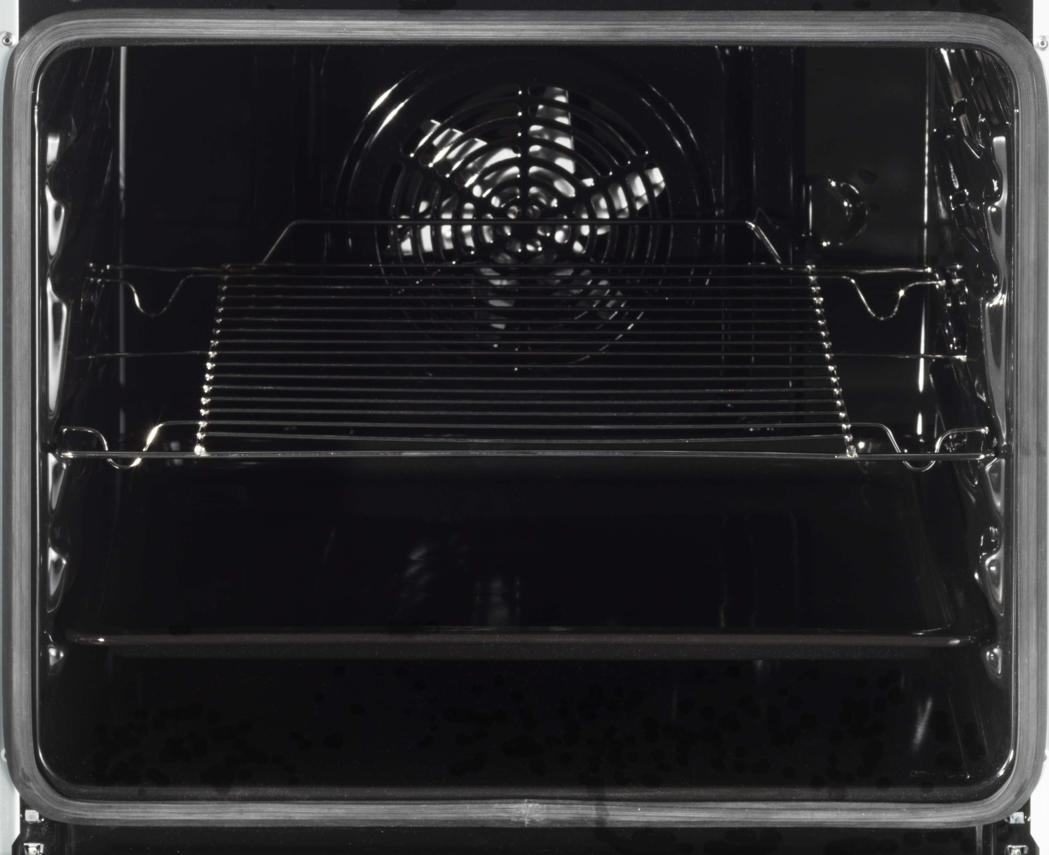 Ein offener Backofeninnenraum. Der Ofen hat Gestelle und einen Ventilator hinten. Das Innere ist dunkel.