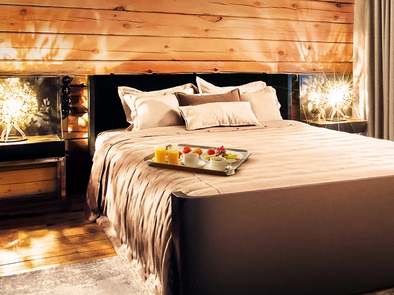 Camera da letto con parete in legno e letto con vassoio per la colazione. Lampade ai lati.