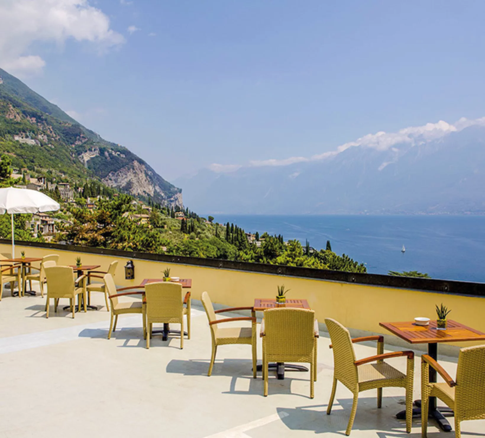Scena di ristorante all'aperto con tavoli, sedie e vista sul lago e sulle montagne.