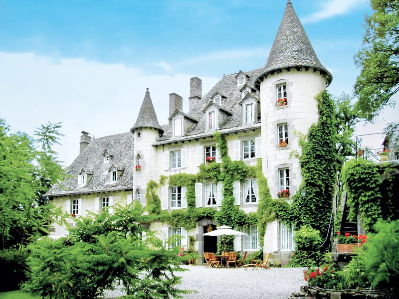 Grand bâtiment blanc avec tourelles, lierre vert et arbres, sous ciel bleu.